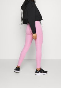 Černá zkrácená mikina s kapucí a růžové legíny, hladká textura, přiléhavý střih, doplněné o černé sportovní boty s bílým logem.