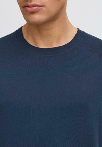 Tricou din bumbac de culoare bleumarin, cu un design clasic de gât rotund, textură fină și mâneci scurte. Stil simplu, fără ornamente.