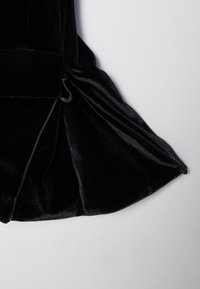 Fragmento de vestido de terciopelo negro con dobladillo acampanado, textura suave y cremallera lateral. La tela tiene un ligero brillo.