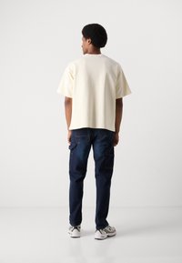 Lys beige kortærmet top parret med mørkeblå cargo jeans. Outfitet har en afslappet pasform og er komplementeret af hvide træningssko.