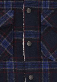 Camisa de cuadros en colores marino, azul y rojo, con una suave textura de lana, dos bolsillos en el pecho y botones metálicos.