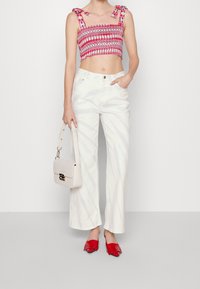 Top cortado smock rojo y blanco con tirantes atados, combinado con pantalones de pierna ancha blancos de tiro alto que presentan sutiles rayas texturizadas. Zapatos de tacón rojos.