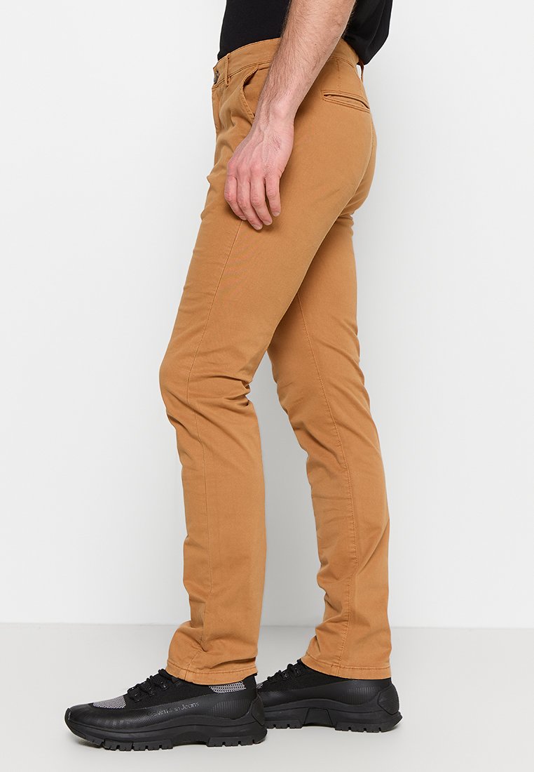 Beżowe bawełniane chinosy o slim fit, z bocznymi i tylnymi kieszeniami, połączone z czarnymi butami sportowymi o teksturowanych podeszwach.