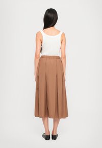 Brun plissert midiskjørt med elastisk linning, sammen med en hvit ermeløs topp, brukt med svarte leiligheter. Minimalistisk design.