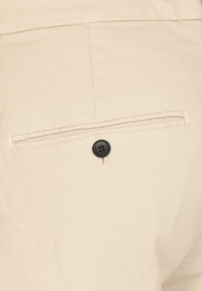 Tessuto beige testurizzato con una tasca posteriore dotata di chiusura a bottone nero e bordo cucito. Design semplice, dettagli minimi.