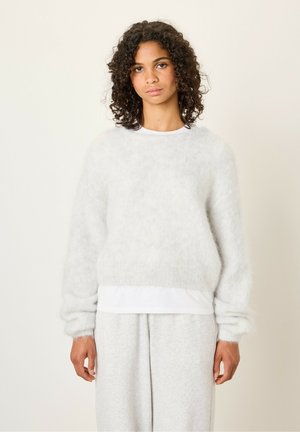 Pull gris clair et duveteux à manches longues et col rond. Superposé sur une chemise blanche ; porté avec un bas gris clair. Texture douce.