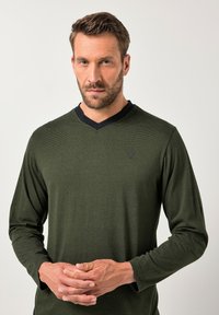 Camisa de manga larga verde oliva con cuello en V negro, que presenta un sutil patrón a rayas y un logotipo grabado en el pecho.