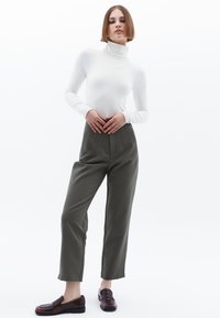 Vit långärmad polotröja som matchas med högmidjade, raka olivgröna byxor och mörkbruna loafers. Minimalistisk design.