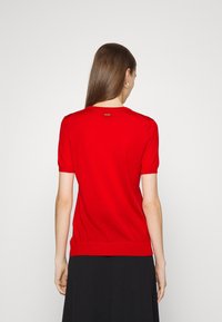 Top corto a maniche corte rosso lavorato a maglia con scollatura tonda, orlo a coste e dettaglio del marchio sul retro, abbinato a un pantalone nero.