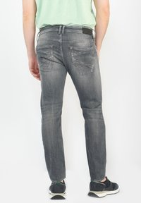 Grå denimjeans med smal passform, med bakfickor och en svart läderlapp vid midjan. Matchas med svarta sneakers.
