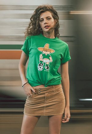 Groene katoenen t-shirt met een cartoonfiguur in een sombrero en voetbaloutfit. Model draagt een beige corduroy minirok.