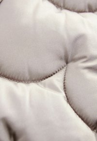 Quiltet stof i en blød beige farve, med en glat tekstur og runde former, synlige sømme og en let glans.