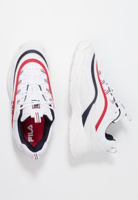 Zapatillas deportivas blancas con acentos en rojo y azul marino, materiales de cuero liso y malla, punta redonda y suelas acolchadas con detalles texturizados.