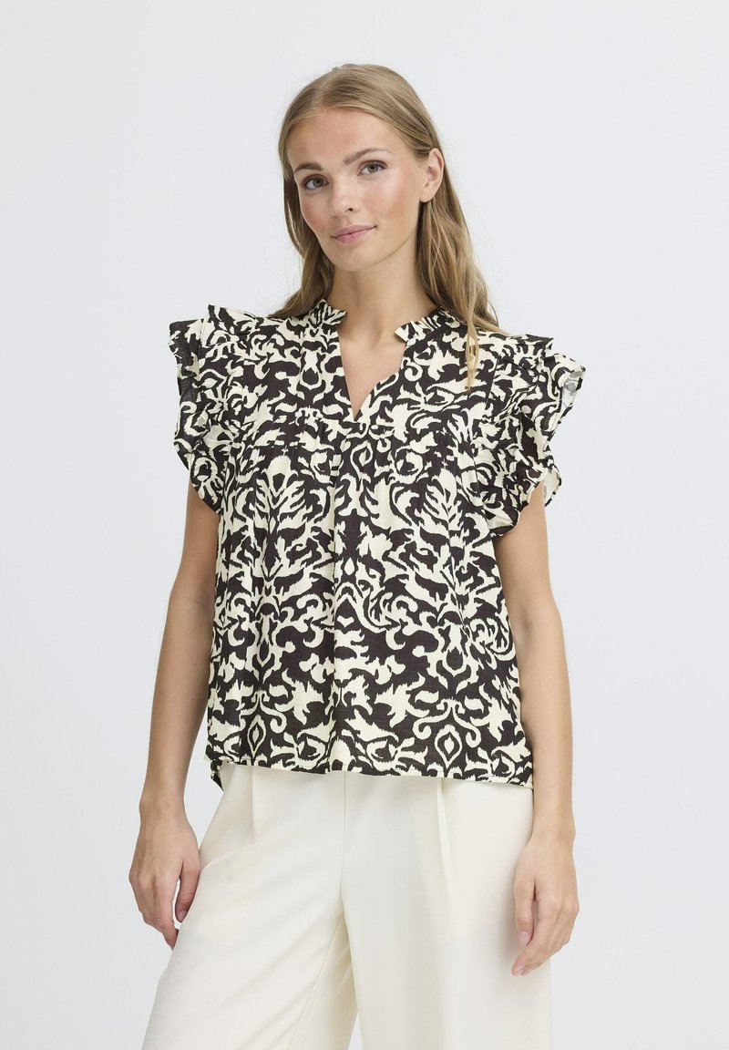 Blusa con motivo floreale nero e crema, con maniche a volant, scollatura a V e vestibilità morbida, abbinata a pantaloni di colore chiaro.