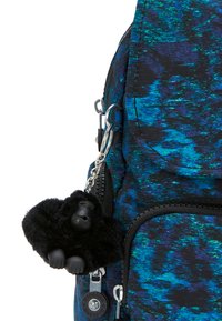 Blå och svart mönstrad ryggsäck med framfickan med dragkedja, som har en liten svart gorillaplushnyckelring fäst vid dragkedjan.
