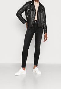 Chaqueta de moto de cuero negro, cuello alto beige ajustado, jeans pitillo negros y zapatillas blancas. Diseño minimalista, textura suave.