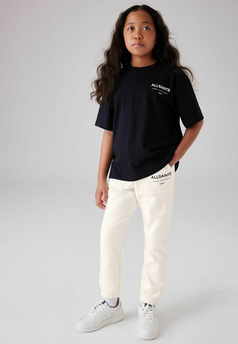 Sort kortærmet T-shirt med hvid "ALLSAINTS" logo, kombineret med hvide sweatpants med et matchende logo ved lommen og opsmøgede hems.