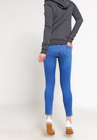 Felpa con cappuccio grigio scuro abbinata a jeans skinny azzurri. I jeans presentano un classico design a cinque tasche e dettagli di cucitura sottili.