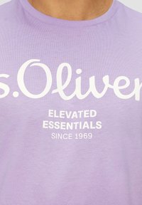 Fialové tričko s krátkým rukávem vyrobené z bavlny, s bílým potiskem textu: "s.Oliver ELEVATED ESSENTIALS SINCE 1969" v ležérním písmu.