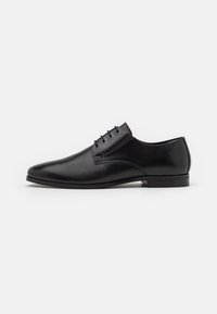 Chaussure habillée en cuir noir avec une finition lisse, un bout pointu, un design à lacets et un talon bas et plat. Présente des accents de couture minimalistes.