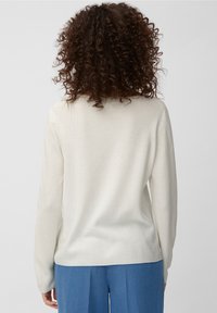 Ljus beige tröja med strukturerad stickad tyg, långa ärmar och rund halsringning, bärs över lösa blå byxor.