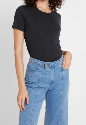 Maglietta nera a maniche corte con scollatura rotonda e dettagli di borchie sulle spalle, abbinata a jeans azzurri a vita alta con una vestibilità comoda.