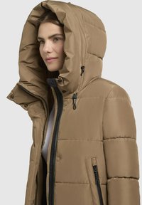 Hnedá púmovo bunda s veľkou kapucňou, so zipsom vpredu, patentkami a bočnými vreckami. Hladká tkanina s prešívanou textúrou.