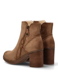 Botines de ante marrón con cierre de cremallera y costuras decorativas. Presentan un tacón de madera apilado y un diseño de punta redonda.
