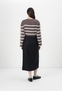 Brun og kremstripet langermet topp parret med et svart midilengde skjørt. Glatte teksturer og minimalistisk design med subtile detaljer.