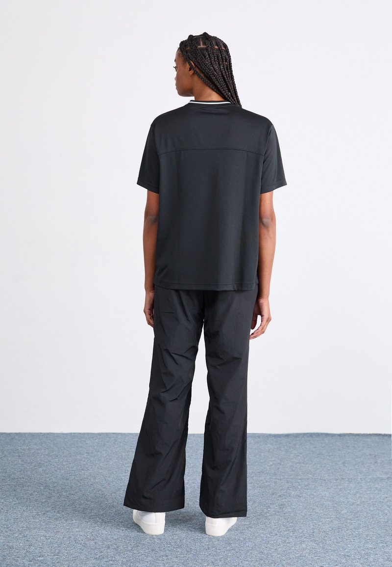 Haut noir à manches courtes avec une coupe droite, associé à un pantalon noir ample. Les deux vêtements ont une texture lisse, sur un fond neutre.