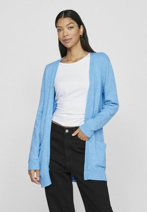Lichtblauwe cardigan van zacht gebreid stof, met een open voorkant, geribbelde manchetten en zijzakken, gedragen over een witte top en zwarte broek.