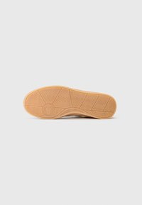 Suola di scarpa in gomma beige con un motivo a zigzag testurizzato e logo circolare, con bordi arrotondati e una superficie liscia e piatta.