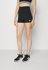 Pantaloni scurți sport negri, cu talie înaltă și o croială strânsă, având logo-ul Adidas. Purtați cu pantofi atletici negri și un top scurt contrastant.