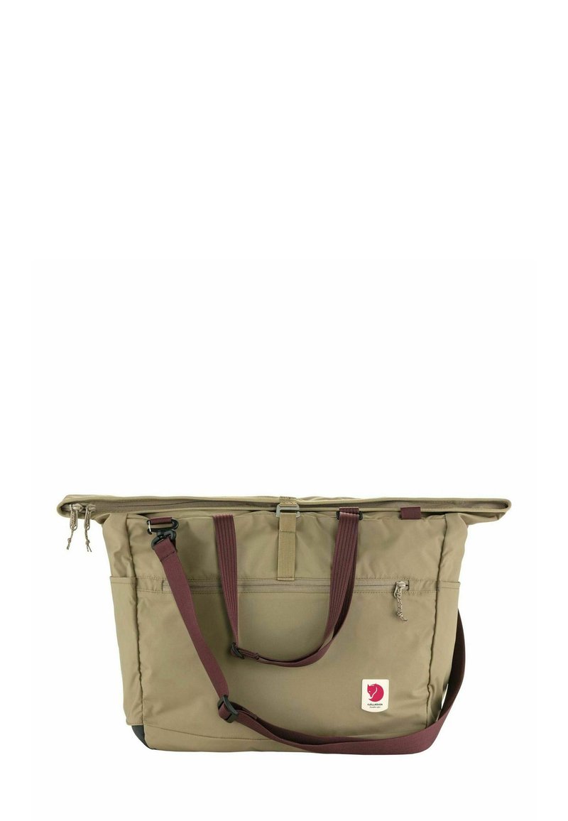 Beige draagtas van nylon, met een ritssluiting aan de bovenkant, leren handvatten, een zijvak en een klein logo op de voorkant.