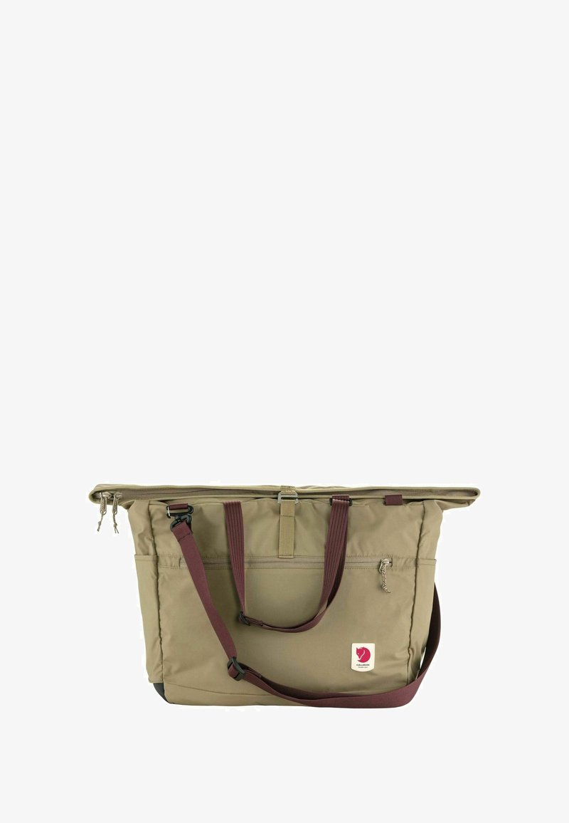 Beige draagtas van nylon, met een ritssluiting aan de bovenkant, leren handvatten, een zijvak en een klein logo op de voorkant.