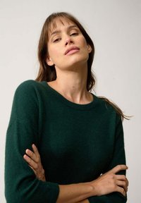 Maglione verde scuro con una consistenza morbida, scollatura rotonda e maniche a tre quarti. Presenta una vestibilità rilassata e un design minimalista.