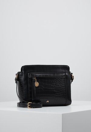 Czarna torebka na ramię z tłoczeniem imitującym skórę krokodyla, z przednią kieszenią na suwak, złotymi elementami i regulowanym paskiem na białym tle.