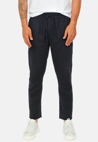 Pantaloni di lino blu navy con una vestibilità rilassata, fascia elastica in vita e dettaglio con coulisse, abbinati a sneakers bianche. Tessuto testurizzato con linee pulite.