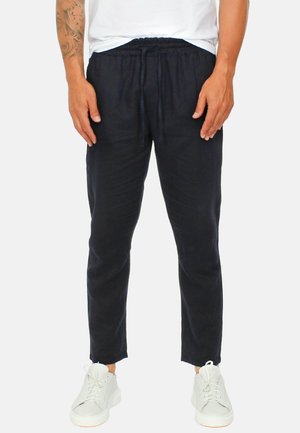 Pantaloni di lino blu navy con una vestibilità rilassata, fascia elastica in vita e dettaglio con coulisse, abbinati a sneakers bianche. Tessuto testurizzato con linee pulite.