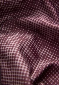 Nahaufnahme von lila Stoff mit einem Muster aus kleinen dunkelbraunen Punkten und Rautenformen, der Falten und Textur zeigt.