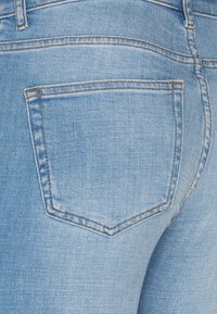 Jeans de mezclilla de color azul claro con un único bolsillo trasero con costuras cosidas y una ligera textura. Diseño suave y ajustado.