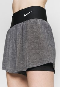 Grijze sportrok met geïntegreerde zwarte shorts, voorzien van een brede zwarte tailleband en een klein wit logo aan de voorkant. Zachte, gestructureerde stof.