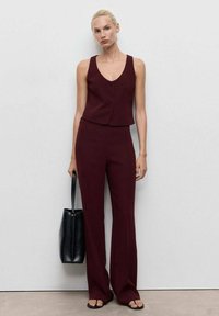 Burgundy ärmlös väst med tre knappar, i kombination med matchande utsvängda byxor. Tillbehören inkluderar en svart tote-väska och sandaletter med öppen tå.