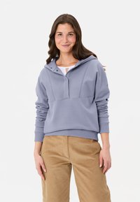 Hellgrauer Hoodie mit einem Viertelreißverschluss-Design, gerippten Bündchen und Saum. Kombiniert mit beigen Cordhose, die eine glatte Textur haben.