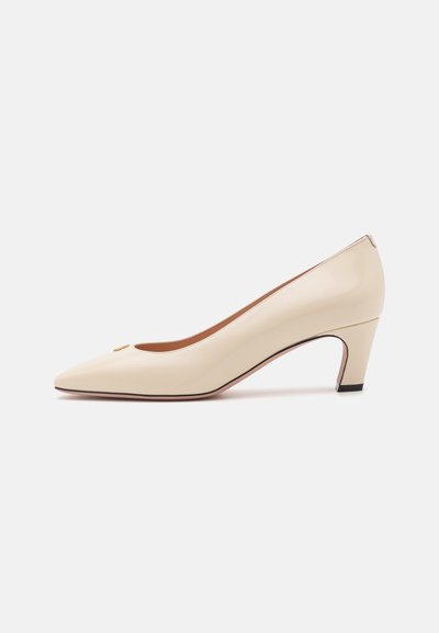Escarpin en cuir verni beige avec un bout pointu et un petit talon carré. Présente un petit logo doré sur le bout. Texture lisse.
