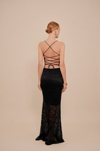 Μαύρο δαντελένιο φόρεμα για το βράδυ με χαμηλή πλάτη και σταυρωτές τιράντες, εφαρμοστή σιλουέτα και φούστα με φαρδύ τελείωμα από διάφανη ύφανση.