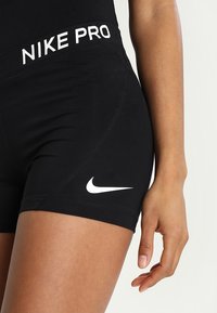 Czarne sportowe szorty z grubym pasem ze znakiem "NIKE PRO". Posiadają kontrastowe białe logo Nike na dolnej lewej stronie. Gładka tekstura.