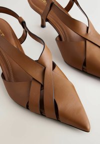 Brūnas ādas sandales ar atvērtu papēdi, smailiem purngaliem, krusteniski pārklātām siksniņām un plānu papēdi. Gluda tekstūra ar izšūšanas detaļām.