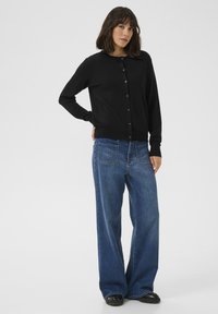Cardigan nero lavorato a maglia con scollo rotondo e chiusura a bottoni, abbinato a jeans in denim blu a vestibilità ampia con lavaggio chiaro.