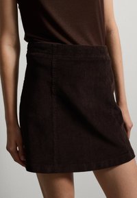 Minifalda de pana marrón con textura de costillas verticales, cintura ajustada y silueta recta, con un dobladillo limpio y sin acentos visibles.
